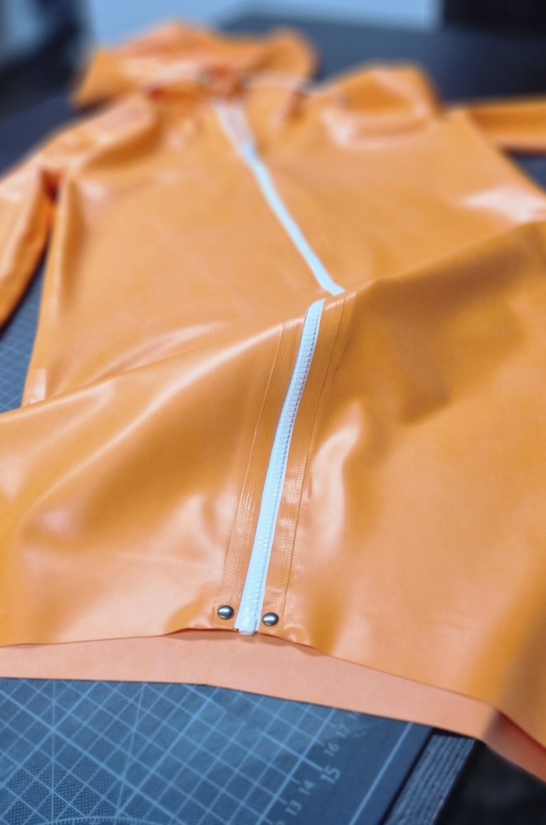 Kapuzenkleid aus Latex. Ein oranges Kapuzenkleid aus Latex mit weißem Reißverschluss.