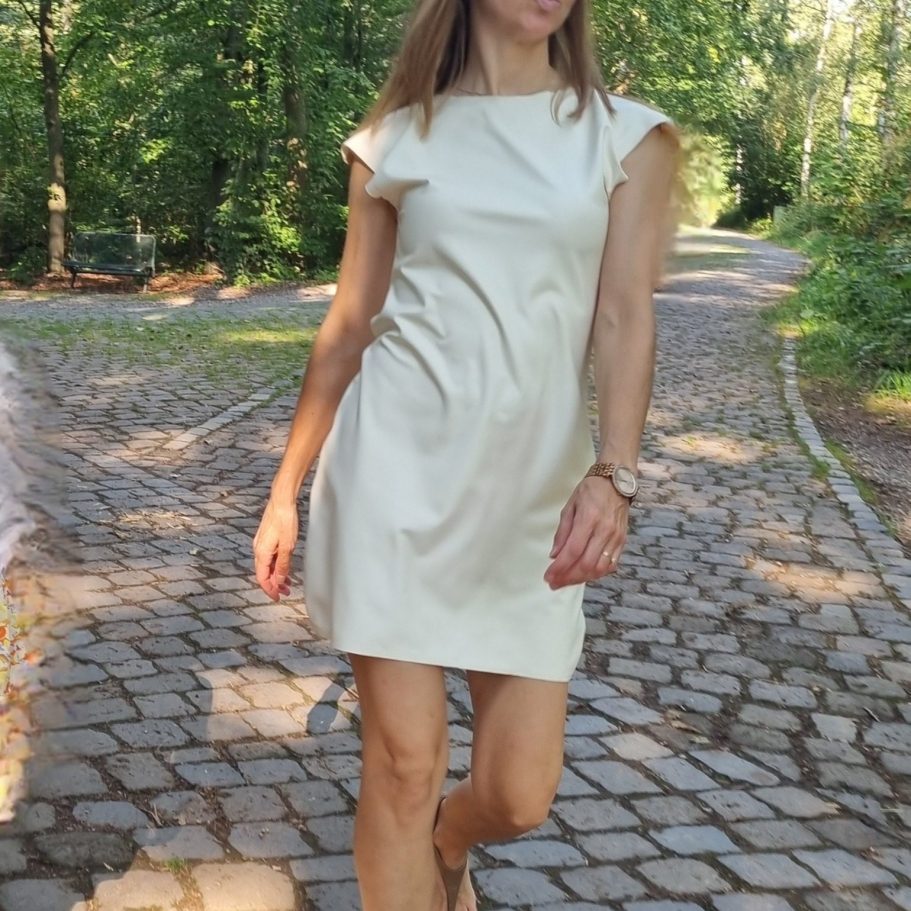 Latexkleid cremefarben, kombiniert mit goldener Uhr und schwarzen Sandalen.